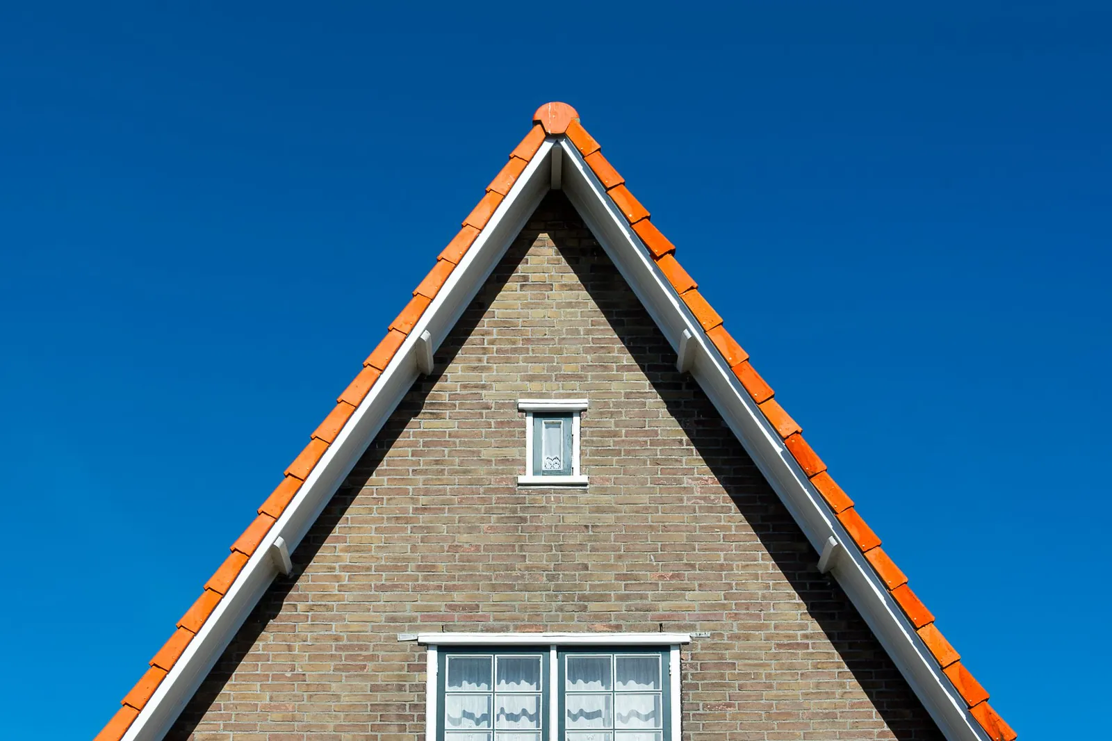 Kopgevel van een bakstenen woning met windveren langs het pannendak